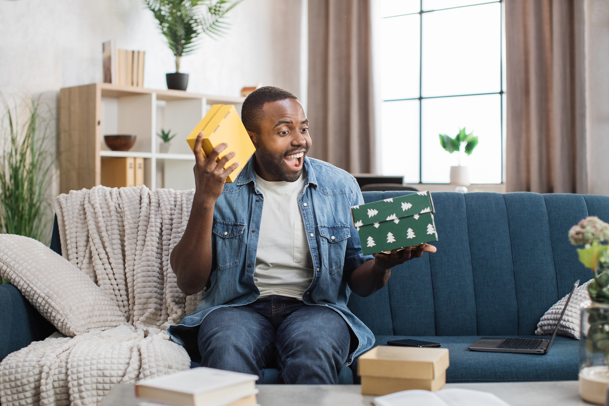 Excited african guy opening gift boxes on couch